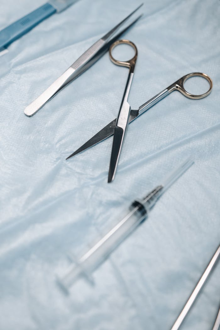 Close-up of surgical scissors, tweezers, and syringe on sterile drapes.